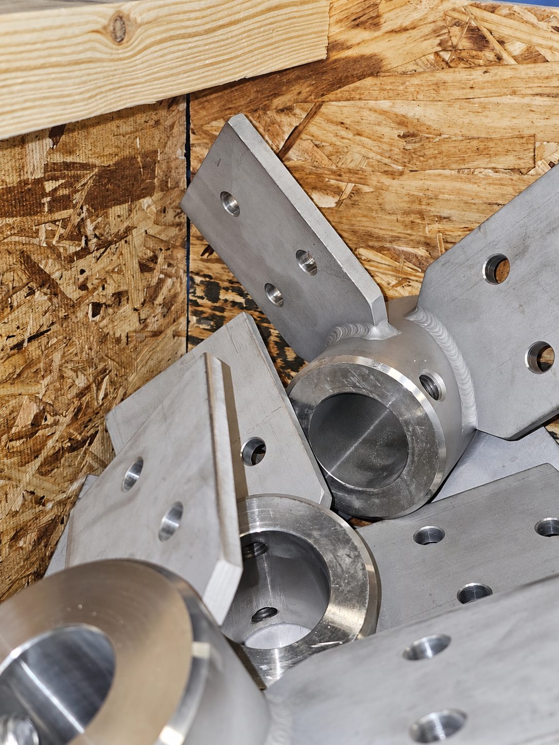 Several machined impeller hubs in a wooden crate, each a bored and counterbored hub with flat blade arms welded on and bolt holes drilled through the arms.