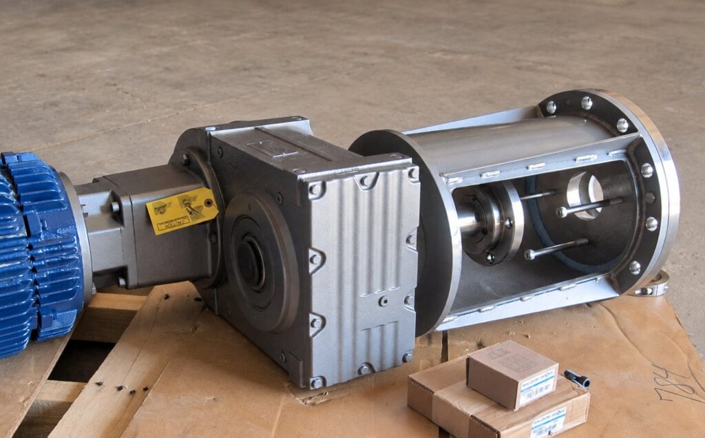 Mixer drive train laid out on a pallet: electric motor, helical gear reducer, open pedestal housing with the shaft coupling visible, and a bolted mounting flange.