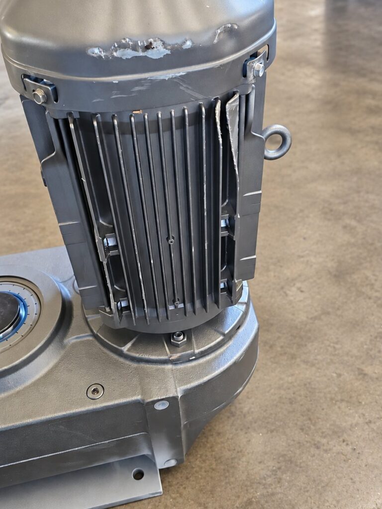 Electric motor bolted to a large cast gear reducer housing with a lifting eye, standing on the shop floor.