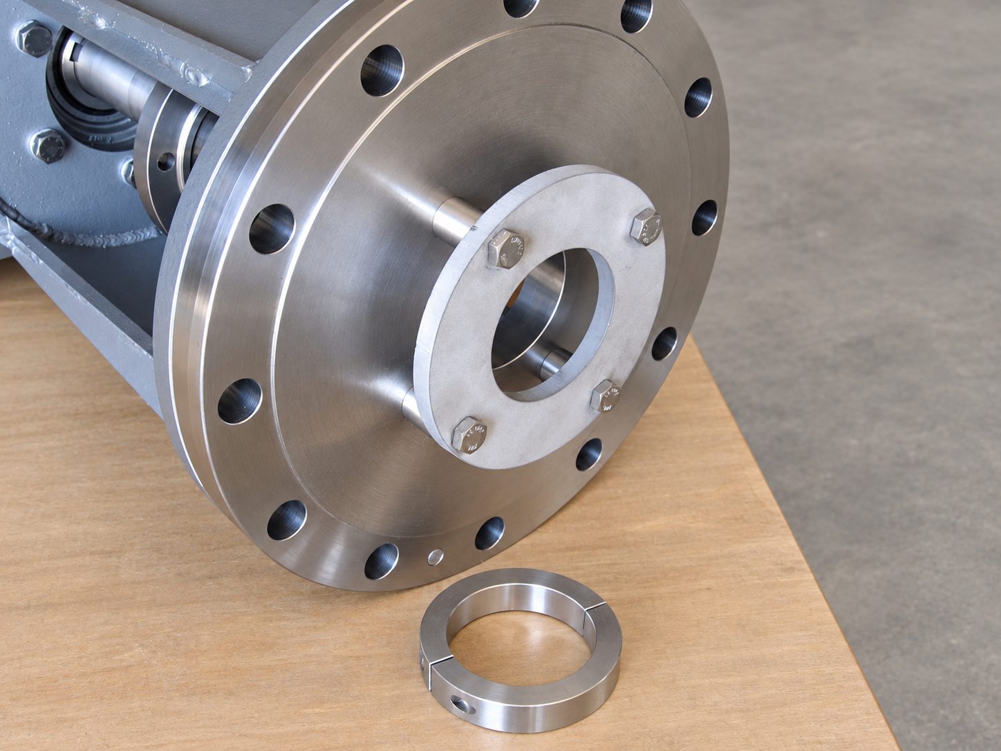 Large machined bolt circle flange on the end of a painted drive housing, with a shaft passing through a bolted split retaining ring, and a two-piece split shaft collar on the bench.