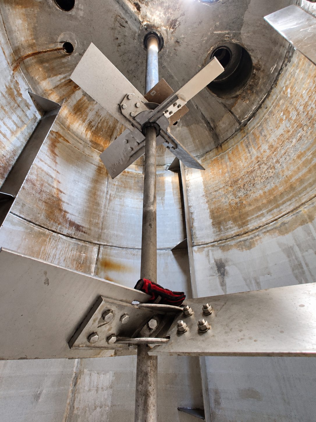View up the inside of a tank at a four-blade pitched blade turbine bolted to a vertical shaft, with wall baffles and a lower bolted hub in the foreground.