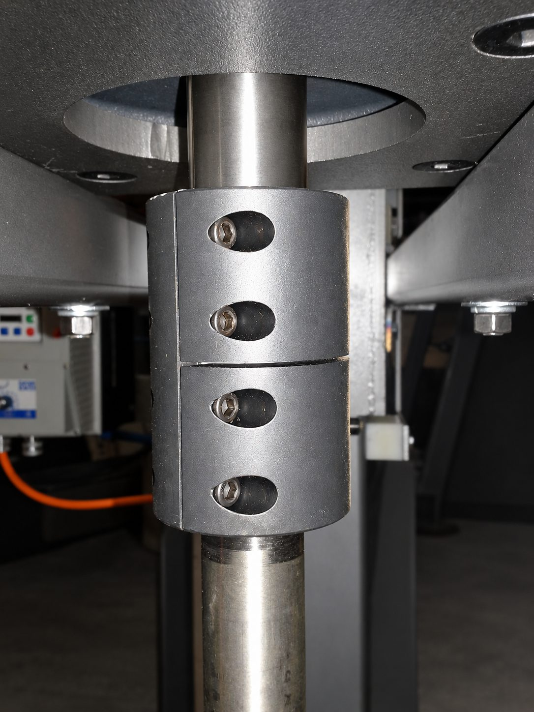 A two-piece rigid clamp coupling with four socket screws joining a drive output shaft above to a mixer shaft below, seen through the opening in the mounting plate.