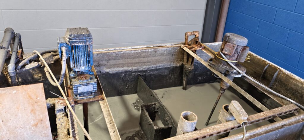 Two small bracket-mounted mixers on the rim of an open rectangular process tank holding a gray slurry, both drives coated in dried product and surface rust.